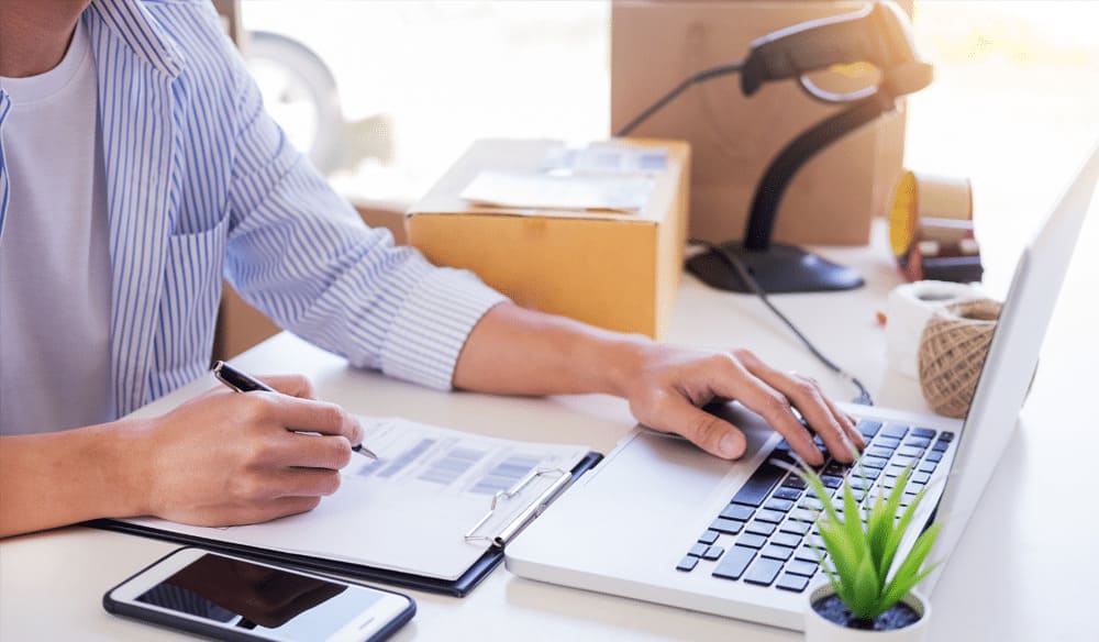 Man working on a laptop while reconciling numbers from a paper.