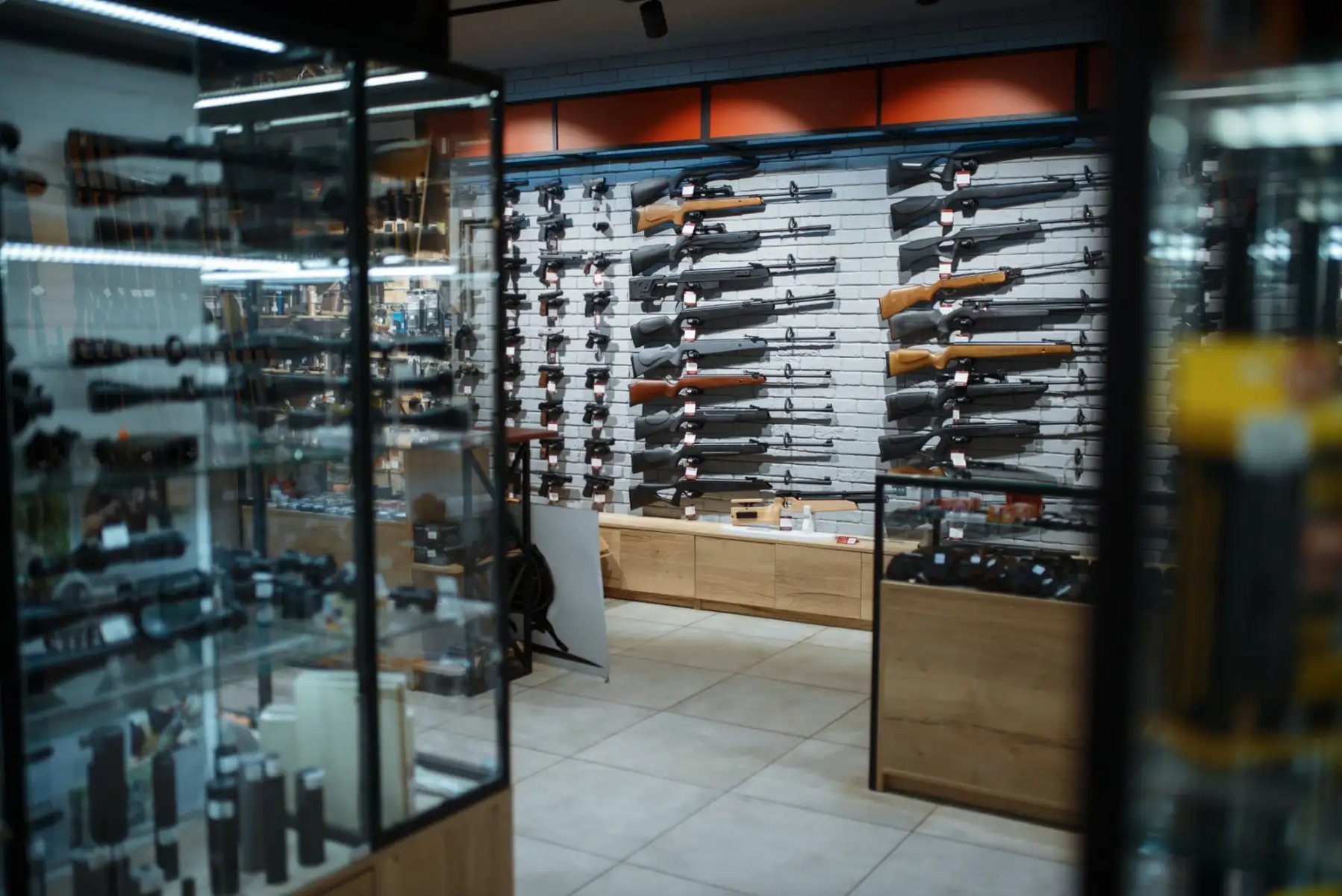 The interior of a firearms retail store with a wall display, glass cases and optics